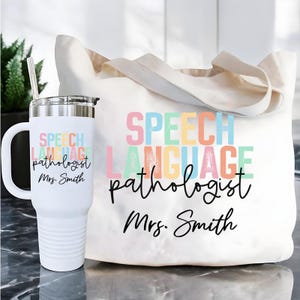 May include: A white tumbler and tote bag set. The tumbler has a handle and a straw. Both items feature the text "SPEECH LANGUAGE pathologist Mrs. Smith" in pastel colors and black script. The tote bag has beige handles.