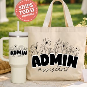 May include: A cream-colored tumbler with a handle and a matching tote bag. Both items feature a black floral design and the words "ADMIN assistant". A round sticker that says "SHIPS TODAY WOMAN OWNED" is in the upper left corner.