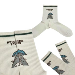 May include: Off-white socks with a green stripe at the top and the text "MY NEIGHBOR TOTORO". The socks feature a cartoon illustration of Totoro holding an umbrella. The socks are ribbed.