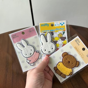 May include: Three embroidered fabric patches featuring Miffy the rabbit and a brown bear character. Each patch is packaged in a clear plastic sleeve with a cardboard backing displaying the text Dick Bruna and Japanese characters.