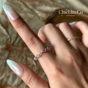May include: A wire-wrapped ring featuring small, round, translucent purple beads, positioned alongside a thin, gold-toned band ring. The image includes the text ChicLiteCo HandmadeJewelry with a line art graphic of a profile silhouette.