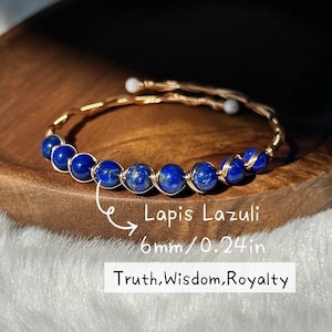 Könnte beinhalten: Ein goldfarbenes Armband mit tiefblauen Lapis Lazuli-Perlen, jede mit einem Durchmesser von 6 mm. Auf dem Armband steht "Truth, Wisdom, Royalty."