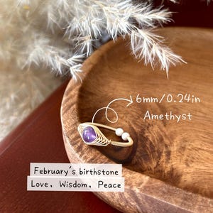 May include: A gold wire-wrapped ring featuring a 6mm (0.24in) amethyst gemstone and two white beads. The ring is set in a wooden bowl. Text on the image reads: February's birthstone, Love, Wisdom, Peace.