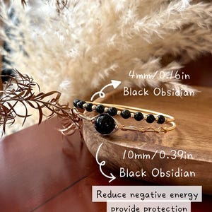 May include: Two gold bracelets with black obsidian beads. One has 4mm beads, the other a larger 10mm bead. The image includes text: "Reduce negative energy provide protection."