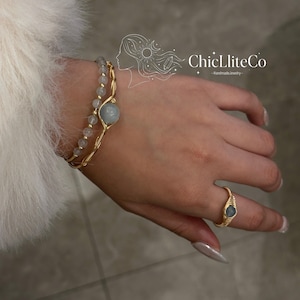 May include: Gold-toned wire-wrapped bracelet and ring set with light blue gemstone accents. The bracelet features a large central stone and smaller beads. The ring has a similar design with a single gemstone. The brand name "ChicLliteCo" is visible.