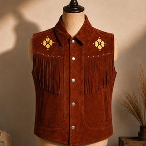 May include: A brown suede vest with a collared neckline and fringe detailing. The vest features two front pockets and is adorned with yellow floral embroidery and silver-tone studs. The vest is buttoned up and displayed on a mannequin.