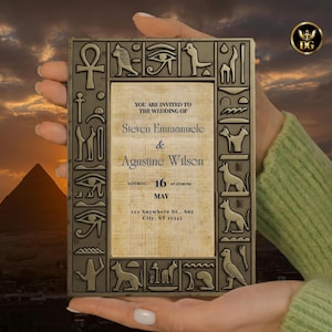 May include: An ornate, rectangular wedding invitation with an ancient Egyptian theme. The bronze-colored frame features hieroglyphic symbols. The invitation text reads "You are invited to the wedding of Steven Emmanuele & Agustine Wilson" with the date and time.
