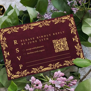 K&ouml;nnte beinhalten: Eine weinrote RSVP-Karte mit goldenen floralen Akzenten und dem Text "PLEASE KINDLY REPLY BY JUNE 25TH". Die Karte enth&auml;lt einen QR-Code und Optionen zur Annahme mit Vergn&uuml;gen oder Ablehnung mit Bedauern. Die Karte ist von gr&uuml;nen Bl&auml;ttern und rosa Bl&uuml;ten umgeben.