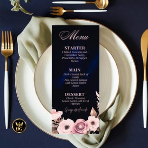 Op de afbeelding: Een formeel menukaart met een donkerblauwe achtergrond en bloemmotieven. Het menu bevat een voorgerecht, hoofdgerecht en dessert. Het menu staat op een wit bord met goudkleurig bestek en een groene servet.