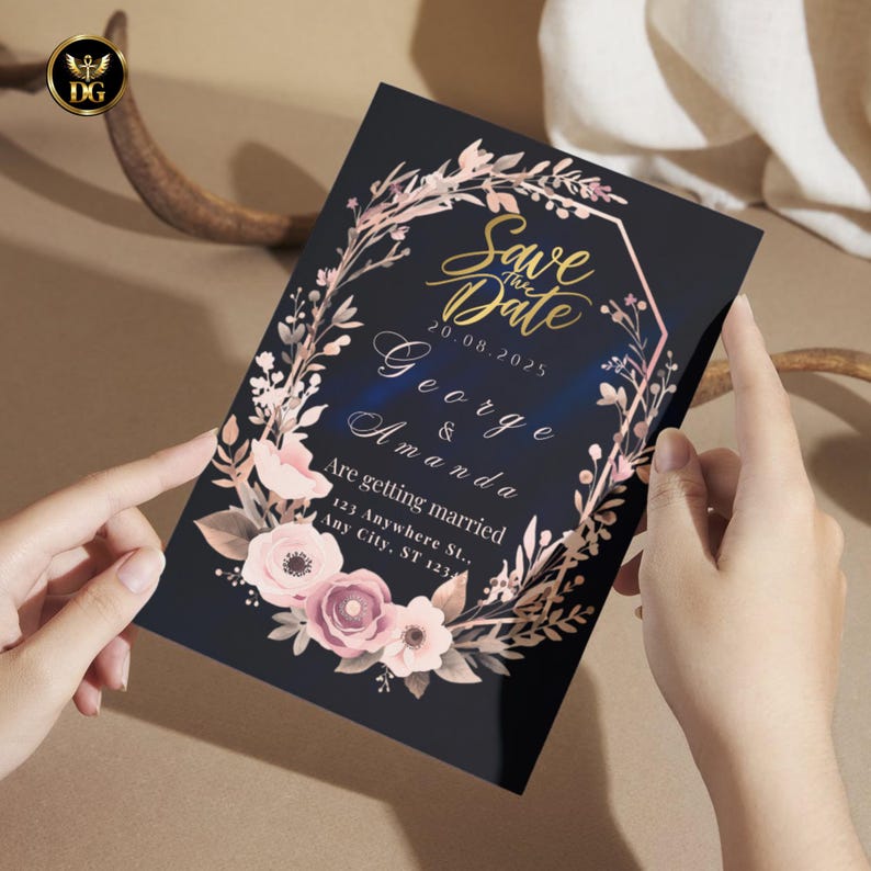 Op de afbeelding: Een zwarte trouwkaart met gouden tekst met de tekst "Save the Date" en de namen "George & Amanda". De uitnodiging is versierd met een bloemenkrans in roze en perziktinten.