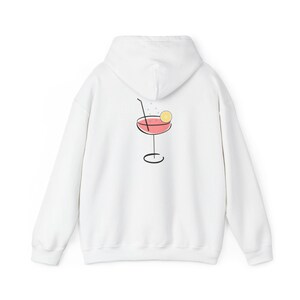 Op de afbeelding: Witte hoodie met een cocktailafbeelding op de achterkant. De afbeelding toont een roze drankje in een glas met een voet, een schijfje citroen en een rietje. Het ontwerp is zwart omlijnd.