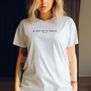Op de afbeelding: Wit T-shirt met de zwarte tekst "SORRY NOT MY PROBLEM", vergezeld van een rood symbool met uitroepteken. Daaronder staat "ERROR_404" in kleinere zwarte letters. Het shirt is een casual stijl met korte mouwen.