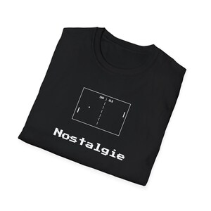 Op de afbeelding: Zwart T-shirt met een witte afbeelding van een retro videogame en het woord "Nostalgie" in witte blokletters. De afbeelding toont een vereenvoudigde versie van het klassieke spel Pong.