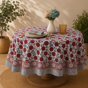 Peut inclure: Une nappe ronde ornée d'un motif répétitif de fleurs rouges et de feuilles bleues sur fond blanc, avec une bordure décorative à motifs floraux et des rayures verticales bleues et blanches. Un vase blanc avec des fleurs est posé dessus.