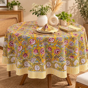 May include: A round tablecloth featuring a vibrant yellow background with a repeating floral pattern in shades of pink, purple, and white. The border displays a distinct yellow and white vertical stripe design, matching the folded napkins on top.
