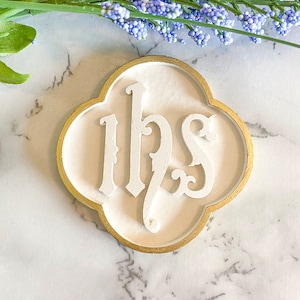 May include: White ceramic plaque with a gold border, featuring the letters "IHS" in a stylized font.