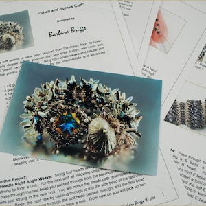 May include: Close-up of a beaded cuff bracelet with a shell and spine design. The cuff is made with a variety of beads, including silver, blue, and white. The cuff is designed by Barbara Briggs.