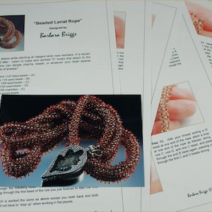 May include: A close-up of a beaded lariat rope necklace made with red, white, and gold beads. The necklace is woven in a right angle weave pattern and has a heart-shaped pendant. The instructions for making the necklace are titled "Beaded Lariat Rope" and are designed by Barbara Briggs.