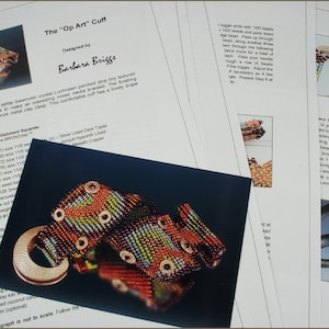 May include: A close-up of a beaded cuff bracelet with a silver metal clasp. The cuff is made with a variety of colors, including orange, green, and brown. The bracelet is designed by Barbara Briggs and is called "The "Op Art" Cuff."