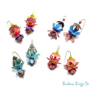 Op de afbeelding: Een verzameling handgemaakte bloemen oorbellen in verschillende kleuren, waaronder roze, blauw, oranje en groen. Elke oorbel heeft een uniek ontwerp met meerdere lagen en texturen, dat een grillige, artistieke stijl laat zien.