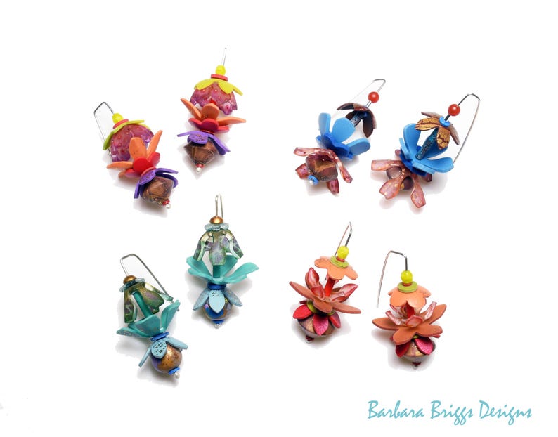 Op de afbeelding: Een verzameling handgemaakte bloemen oorbellen in verschillende kleuren, waaronder roze, blauw, oranje en groen. Elke oorbel heeft een uniek ontwerp met meerdere lagen en texturen, dat een grillige, artistieke stijl laat zien.