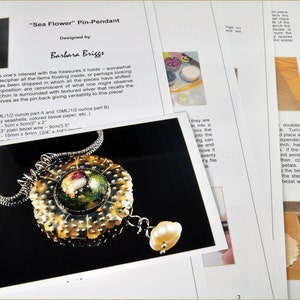 Könnte beinhalten: Ein goldener und silberner Anhänger mit einem Harz-Cabochon, der ein See-Blumen-Design zeigt. Der Anhänger heißt "Sea Flower" und wurde von Barbara Briggs entworfen.