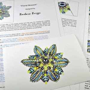 May include: A close-up of a beaded floral brooch with a blue, green, and yellow colour scheme. The brooch is designed by Barbara Briggs and is titled "Floral Brooch".