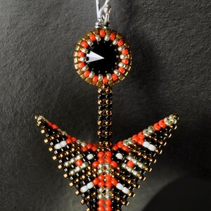 May include: Black, red, gold, and silver beaded earrings with a black crystal in the center. The earrings are shaped like an arrow.