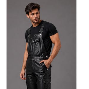 May include: Black leather overalls featuring a front bib pocket with a snap button closure, adjustable shoulder straps with metal buckles, a defined waistband, and side cargo pockets with snap button flaps, worn over a plain black t-shirt.
