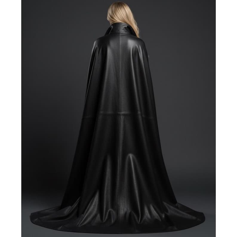 May include: A long, black leather cape with a high collar and a flowing design. The cape is made of a smooth, shiny material and drapes to the floor. The back view shows the cape's full length and elegant silhouette.