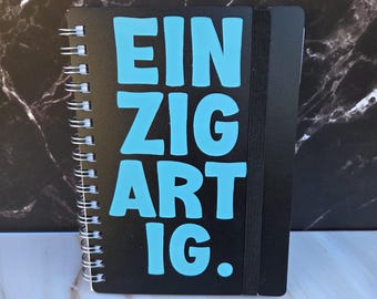 Handmade A6 notebook “UNIQUE.” | Black with light blue vinyl lettering | Lined | 160 pages | Spiral binding