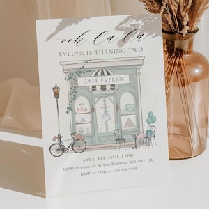 May include: A rectangular birthday invitation card featuring a whimsical illustration of a cafe storefront named CAFÉ EVELYN. The text reads Ooh La La, EVELYN IS TURNING TWO, with event details including the date, time, address, and RSVP phone number.