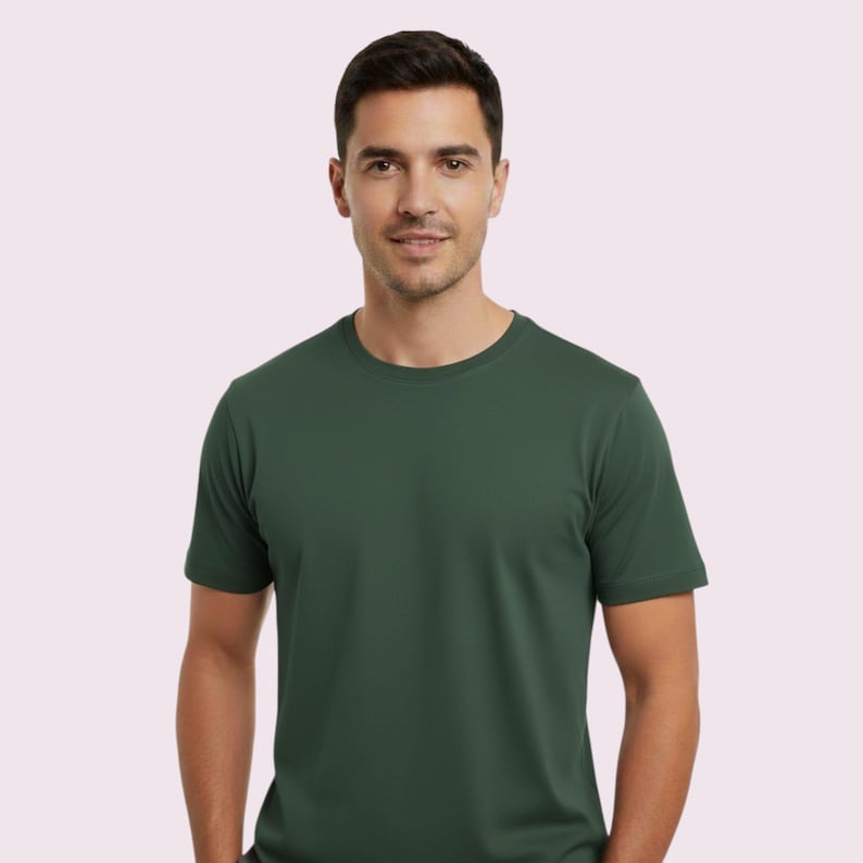 May include: A forest green crew neck t-shirt. The short-sleeved shirt is made of a soft material and is worn by a person. The background is a light pink color.