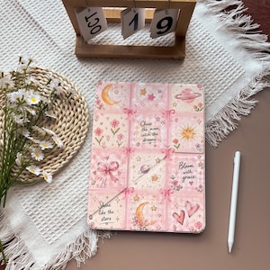 Könnte beinhalten: Eine rechteckige Tablethülle mit einem Raster aus neun rosa Quadraten, verziert mit Illustrationen von Monden, Sternen, Planeten, Blumen, Herzen und Schleifen. Der Text lautet: Chase the moon, catch the dreams, Bloom with grace, Shine like the stars.