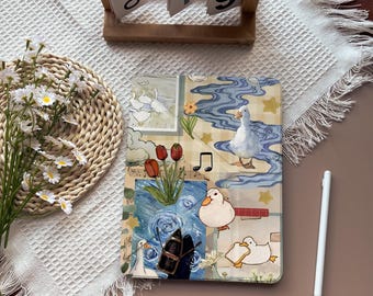 Puede incluir: Una funda decorativa para tableta con un diseño caprichoso de patos, tulipanes y notas musicales. La funda tiene una estética tipo collage con una mezcla de tonos azules, blancos y amarillos. Un lápiz óptico blanco descansa junto a la funda, y un calendario de madera muestra "Oct 19".