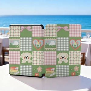 May include: A patterned case for an e-reader, featuring a patchwork design in green, pink, and white. The design includes a bow, a heart with tulips, a cartoon dog, books, and flowers. The case is open, revealing the e-reader screen.