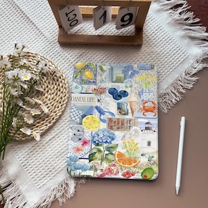 Puede incluir: Una funda decorativa para tableta con un diseño de collage que presenta limones, arándanos, flores y un faro. El texto "COASTAL LIFE" es visible. Un calendario de madera muestra "OCT 19". También hay un lápiz óptico blanco.