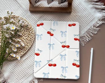 May include: White tablet case with a pattern of red cherries and light blue bows. The case is open, revealing the screen. A white stylus and a wooden calendar are also in the image.