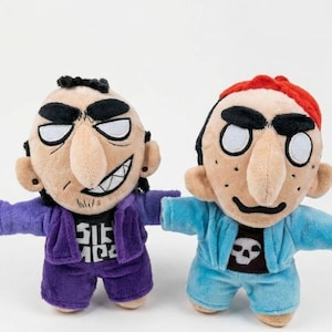 May include: Two plush dolls with large noses and thick eyebrows. The left doll has black hair, a purple jacket, and a black shirt with white text. The right doll has red hair, a light blue jacket, and a black shirt with a white skull graphic.