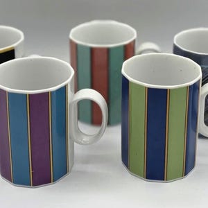 May include: Five ceramic mugs with white handles. The mugs feature various designs, including vertical stripes in blue, green, and purple, and geometric patterns. The mugs are suitable for coffee, tea, or other beverages.