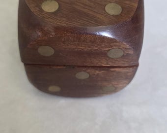 Könnte beinhalten: Eine Würfelbox aus Holz mit Messing-farbenen Punkteinlagen. Die Box ist dunkelbraun und hat eine glatte, polierte Oberfläche. Die Würfelbox hat eine Würfelform mit abgerundeten Kanten.