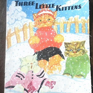 May include: Vintage fabric panel featuring the title "Three Little Kittens" with illustrations of three cats in a snowy scene. The cats are wearing clothing in red, green, and pink. The fabric is labeled "Real Cloth" and includes copyright information.