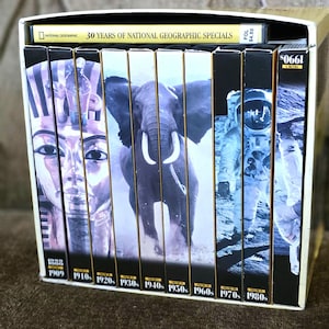 Puede incluir: Una colección de cintas VHS de National Geographic en una caja de cartón. Las cintas presentan imágenes de un faraón egipcio, un elefante, un astronauta y otras escenas. La caja está etiquetada como "30 Years of National Geographic Specials."
