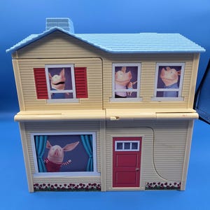 May include: A two-story toy house with a light yellow exterior, blue roof, and red accents. The house features windows with images of a pig character. The front door is red. The house is a children's toy.