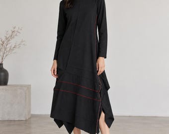Könnte beinhalten: Ein schwarzes, langärmeliges Midikleid mit asymmetrischem Saum und markanten roten Ziernähten an der Seite und den unteren Bahnen. Das Kleidungsstück hat einen Rundhalsausschnitt und eine strukturierte, mehrlagige Silhouette.