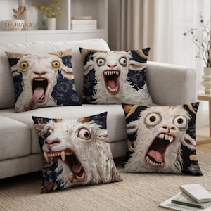 Puede incluir: Cuatro cojines decorativos con diseños de caras de cabras. Las cabras tienen ojos grandes y bocas abiertas, algunas mostrando sus lenguas y dientes. El fondo es un patrón floral azul oscuro. Sobre un sofá gris claro.