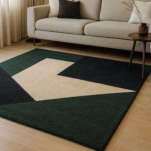 Op de afbeelding: Een modern geometrisch vloerkleed met een patroon van donkergroene, zwarte en beige vormen. Het rechthoekige kleed ligt op een houten vloer. Een beige bank en een bijzettafel zijn zichtbaar op de achtergrond.