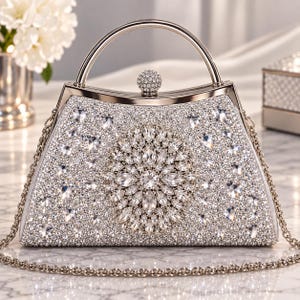 May include: A silver-toned clutch handbag featuring a metallic frame, a top handle, and a detachable chain strap. The exterior is covered in small clear crystals with a large, central floral-shaped cluster of marquise and round cut crystals.