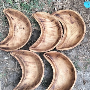 Może przedstawiać: Sześć drewnianych misek w kształcie półksiężyca z naturalnym wykończeniem słojów drewna. Miski są ułożone w grupie, prezentując swój unikalny kształt oraz wariacje w kolorze i fakturze drewna. Miski są prawdopodobnie do serwowania jedzenia.