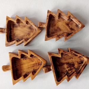 Puede incluir: Cuatro bandejas de madera con forma de árbol. Cada bandeja está tallada en madera y tiene un acabado marrón natural con acentos más oscuros. Las bandejas tienen un asa en un lado y están diseñadas con un área empotrada para sostener artículos.